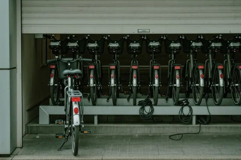 E-bikes standing in a rental rack outside a shop, with chargers on a shelf inside the doorway.
