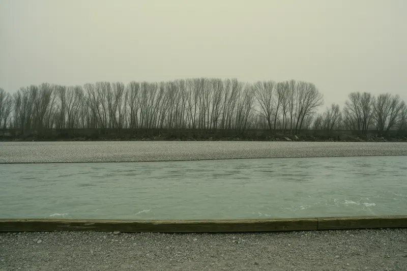 A gravel riverside cycle path beside a fast pale-green river with shingle banks and bare trees along the bank.